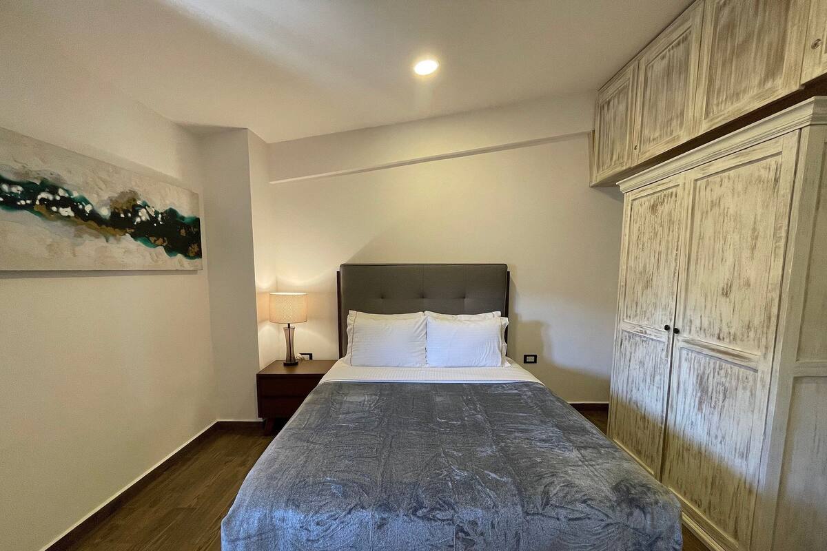 A bedroom with a bed, a nightstand, a lamp, and a wardrobe.