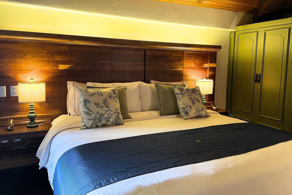 A neatly made bed with floral pillows, a wooden headboard, and a green wardrobe in a hotel room.