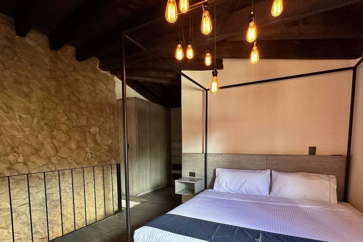 A bedroom with a four-poster bed, a stone wall, and a wooden ceiling.