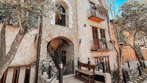 Un edificio de piedra con puertas y balcones de arco, rodeado de árboles y un camino adoquinado.