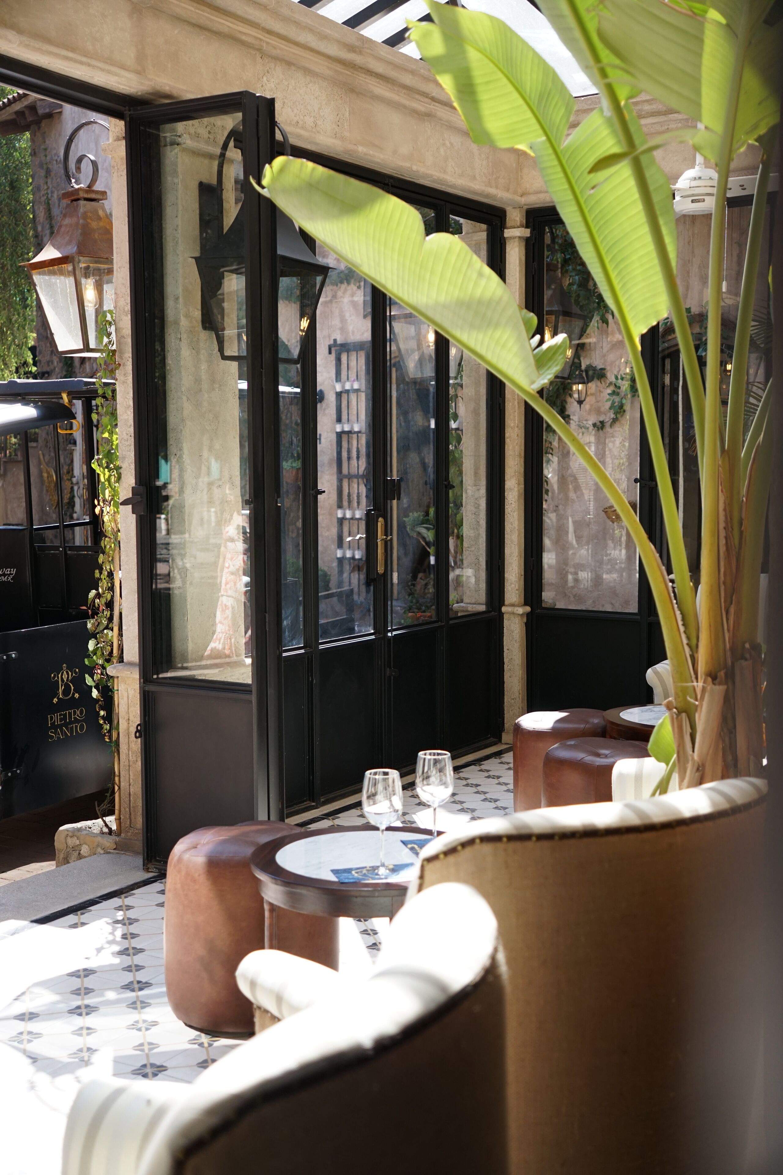 Un restaurante con mesas al aire libre, una planta grande en maceta y vista a la calle a través de un escaparate.