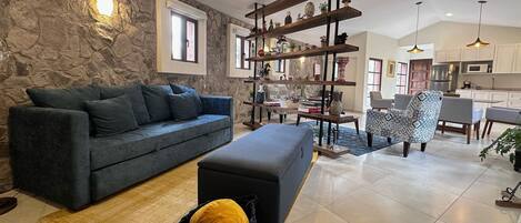 A modern living room with a stone wall, a dark blue sofa, a wooden coffee table, and a kitchen in the background.