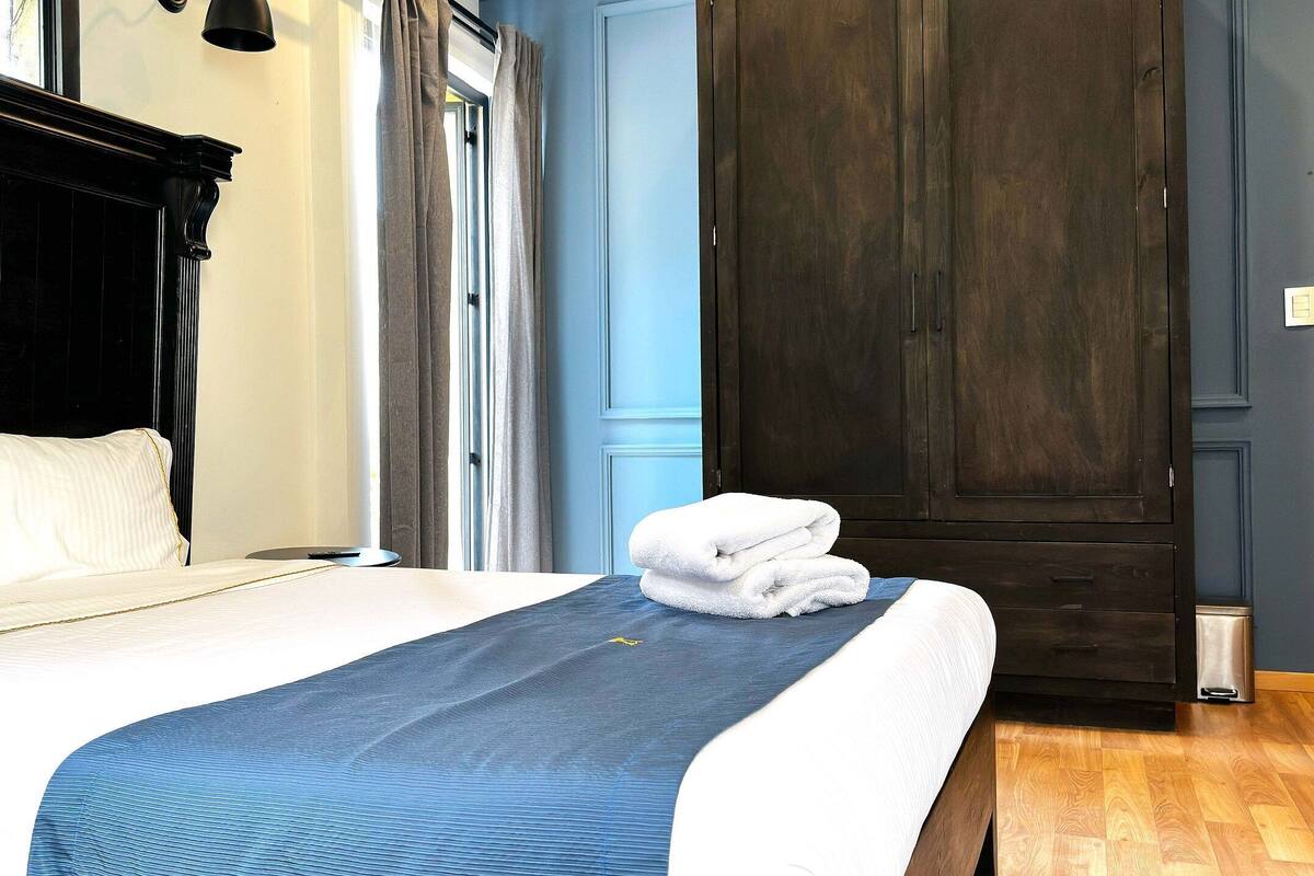 A hotel room with a large bed, a wooden wardrobe, and a window with curtains.
