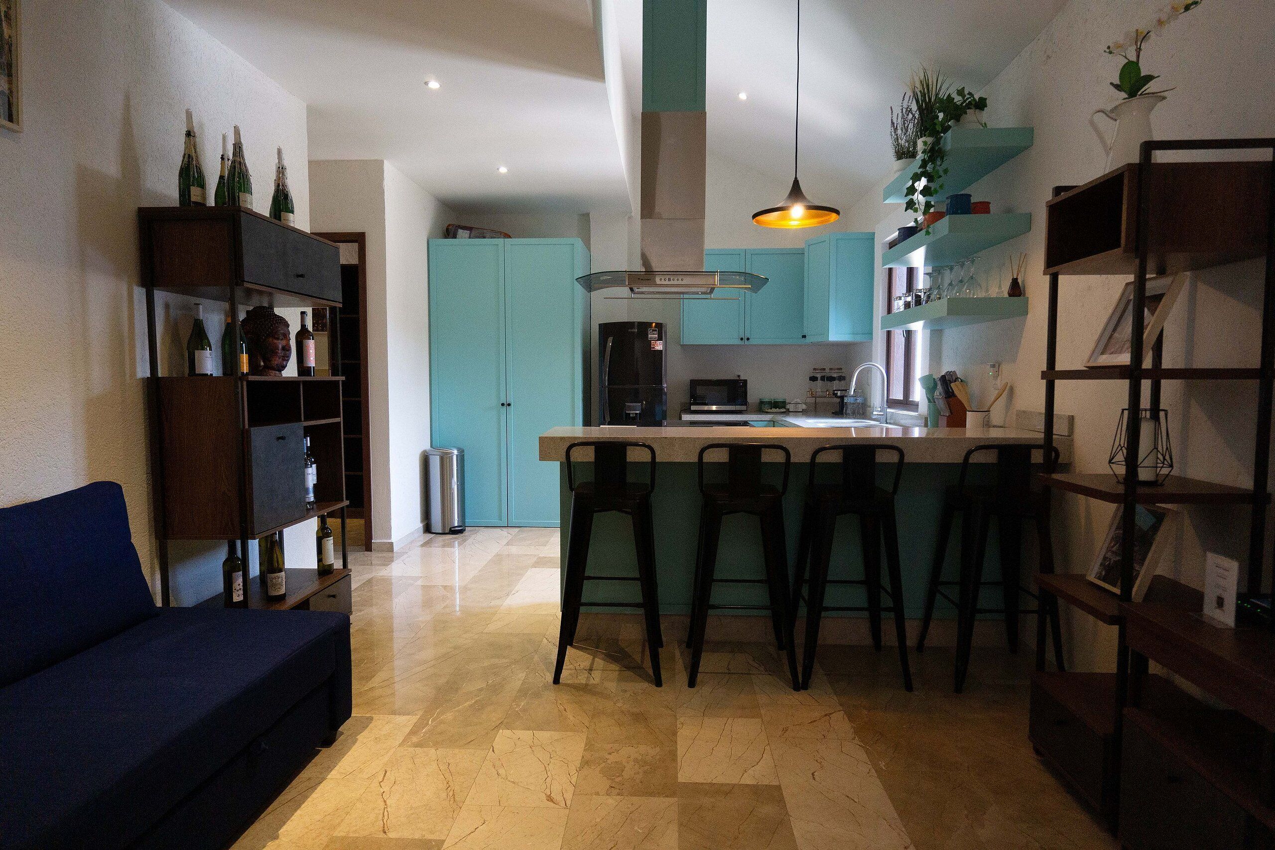 A modern kitchen with a central island, bar stools, and a blue sofa in a living area.