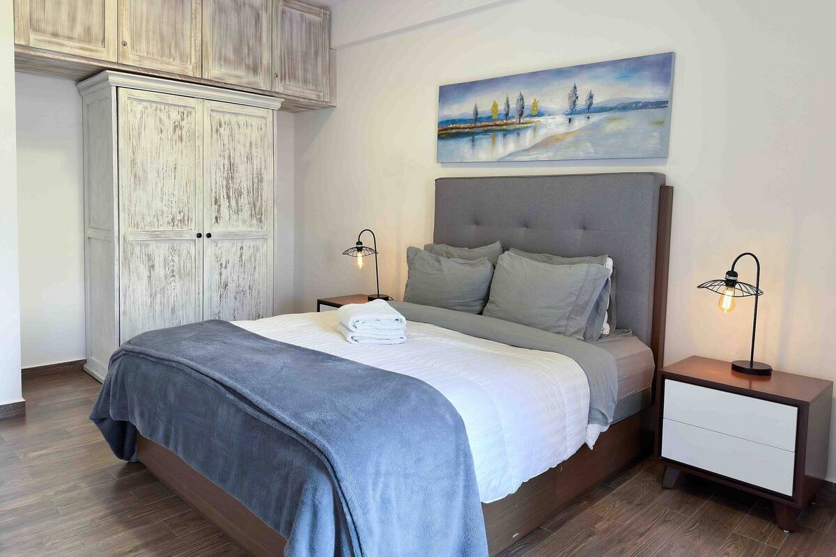 A bedroom with a bed, nightstands, a painting, and a wardrobe.