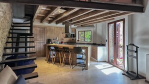 Una cocina moderna con una isla central, taburetes de madera y una escalera que sube a un nivel superior.