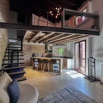 Una cocina moderna con una isla central, taburetes de madera y una escalera que sube a un nivel superior.
