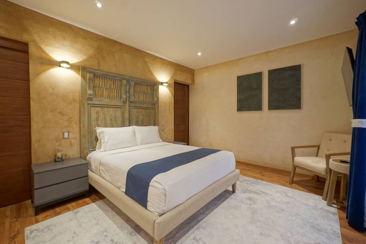 A bedroom with a large bed, bedside tables, a chair, and two wall-mounted lights.