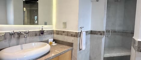 A modern bathroom with a large oval sink, a mirror, a shower, and wooden cabinetry.