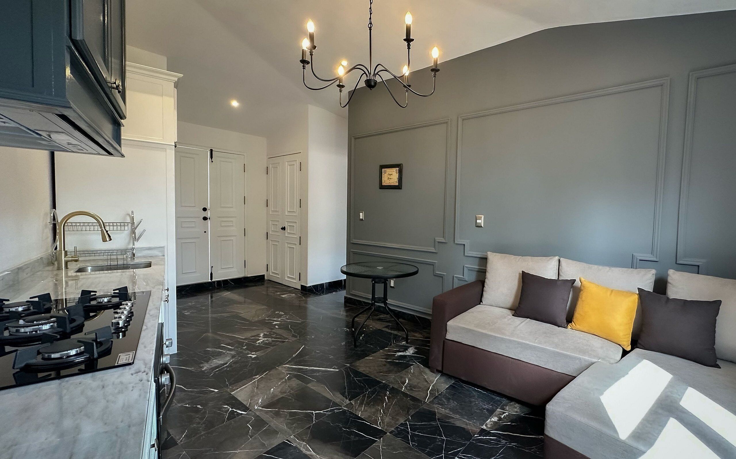 A modern living room with a marble floor, a sofa with cushions, a small round table, and a chandelier.