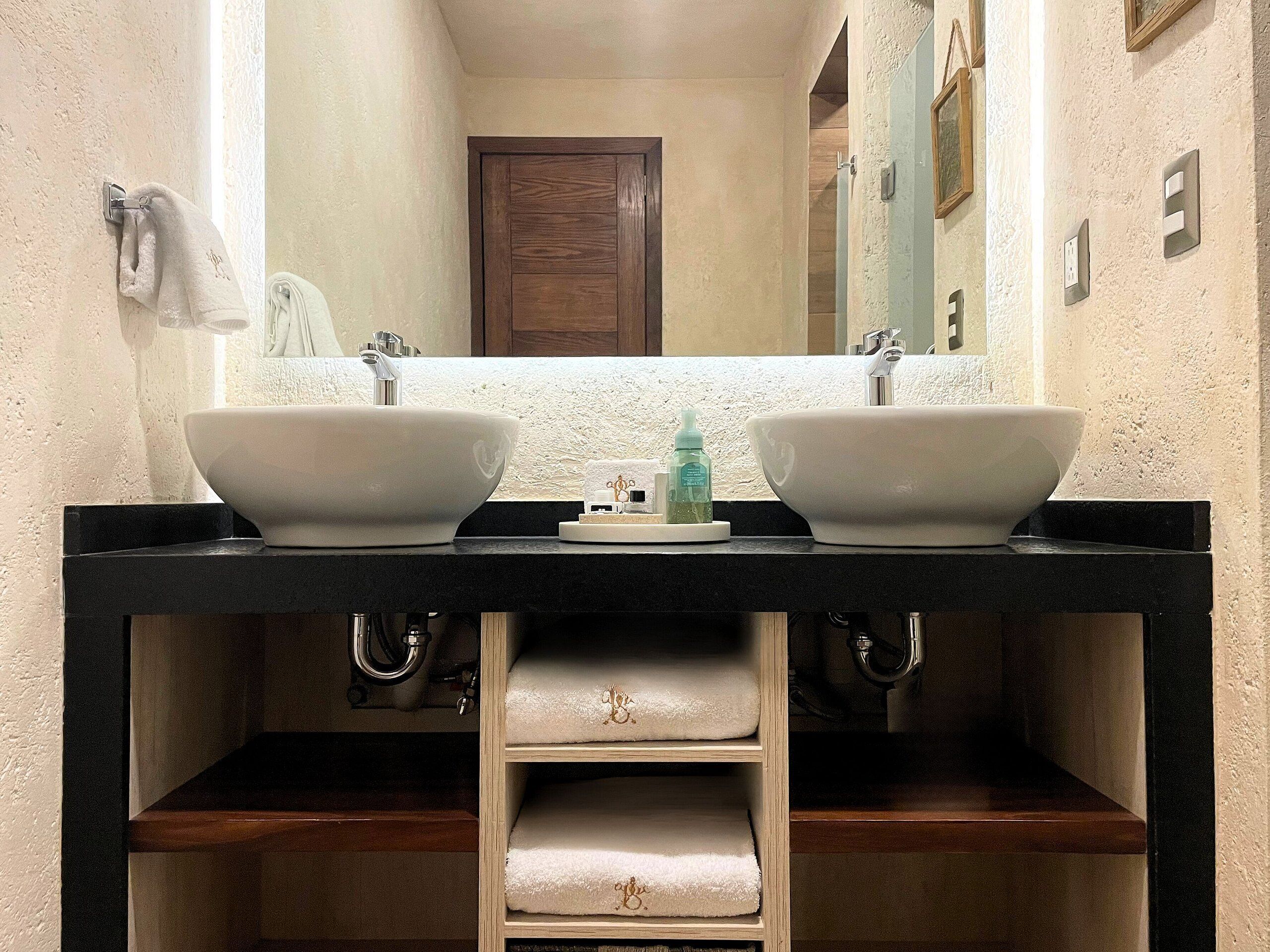 A bathroom with two white sinks, a mirror, and a wooden vanity with shelves.