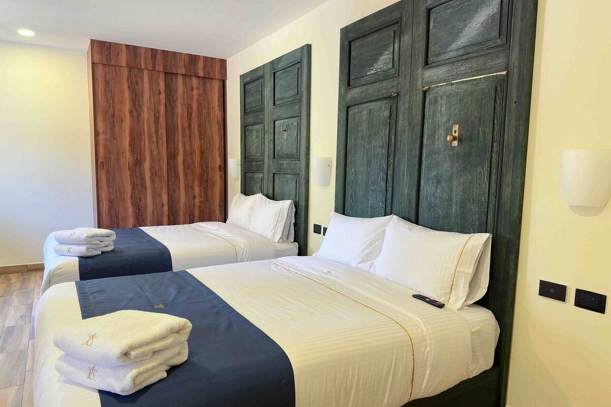 A hotel room with two beds, wooden headboards, and a wooden wardrobe.