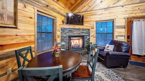 L’intérieur chaleureux d’un chalet avec une cheminée en pierre, des murs en bois, une table à manger et un canapé en cuir.