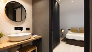 A modern bathroom with a large round mirror, a vessel sink, and a wooden shelf with towels.