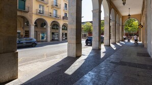A covered pedestrian walkway with stone columns and arches, leading to a building with multiple balconies and windows.