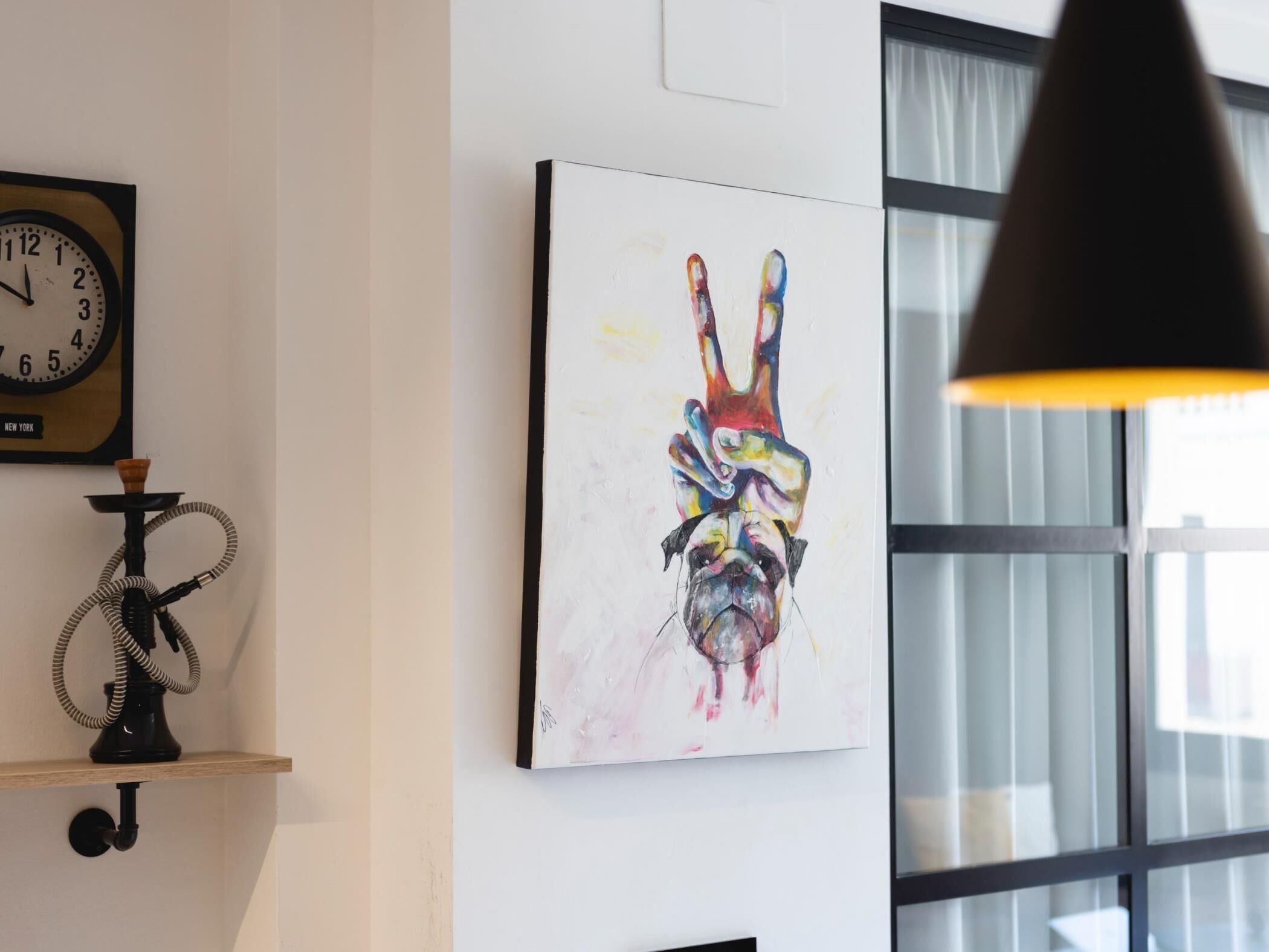 A room with a wall-mounted clock, a colorful abstract painting, and a hookah on a shelf.