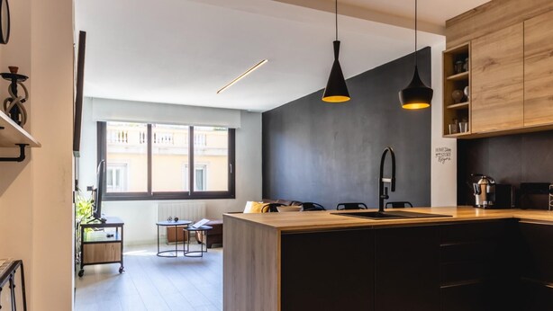 A modern kitchen with a central island, pendant lighting, and a view of the outside balcony.