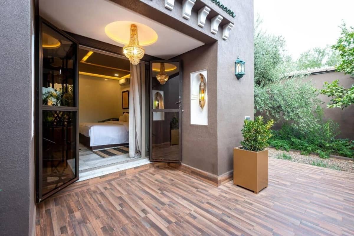 Entrada de hotel con terraza de madera, una planta grande en maceta y un candelabro.