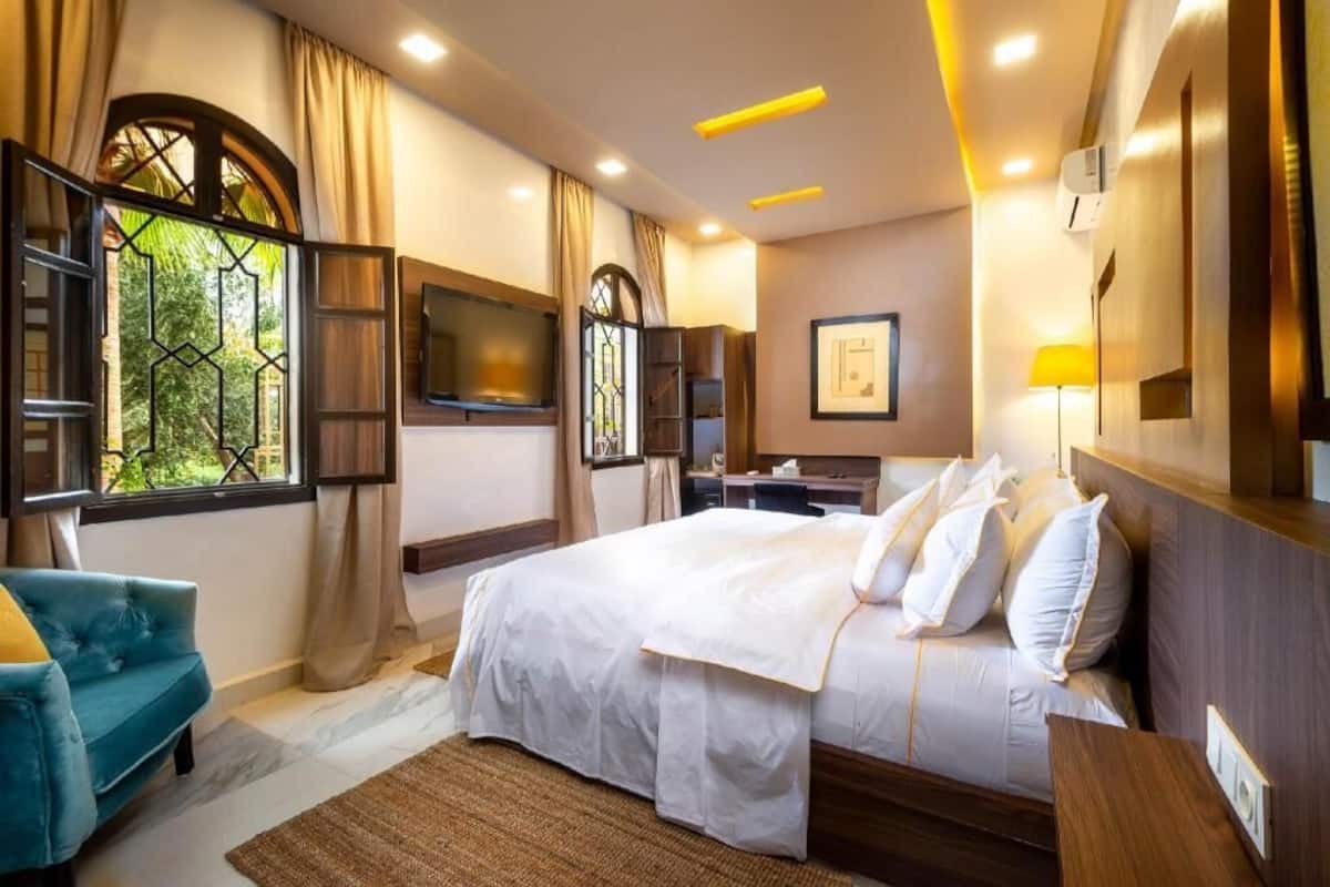 Habitación de hotel con cama, escritorio, televisión, ventana con cortinas y vista a zonas verdes.