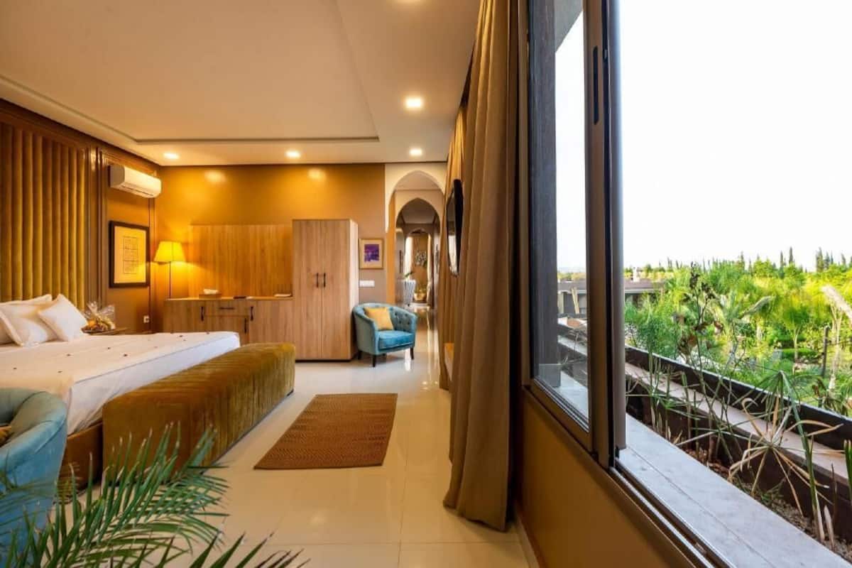 Habitación de hotel con cama, escritorio, silla, ventana con vista a zonas verdes y balcón.