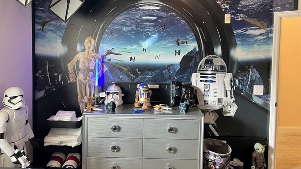 Une pièce décorée d’une fresque murale sur le thème de Star Wars, avec une commode et divers objets de collection relatifs à Star Wars.