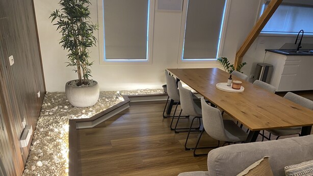 A modern kitchen with a wooden dining table, grey chairs, and a built-in bench.