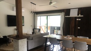 A modern living room with a wooden dining table, grey sofa, and a TV mounted on the wall.