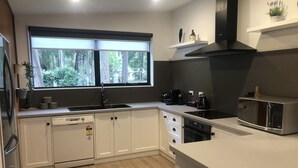A modern kitchen with white cabinets, a black stove, and a window overlooking a forest.