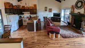Un vaste espace de vie comprenant une cuisine, un plancher en bois, un canapé en cuir rouge, une cheminée et une grande fenêtre.