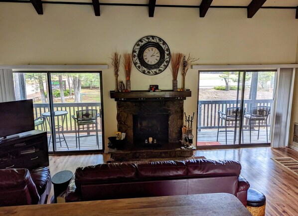 A cozy living room with a stone fireplace, a television, leather sofa, and a large window overlooking a deck. - Beautiful Bell's Bungalow in the heart of the White Mountains , Pinetop AZ! (Pinetop)