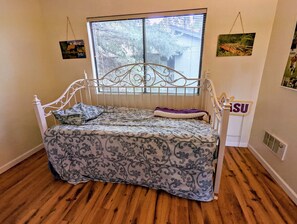 A single bed with a metal headboard, a window with blinds, and a wall-mounted sign.