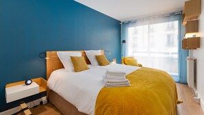 Una camera d'albergo con un letto, un comodino, una finestra con tende e una mensola a parete.