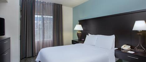 A hotel room with a bed, a TV, a desk with a lamp, and a telephone.