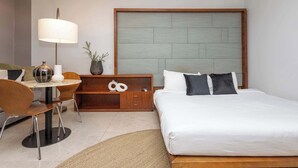 Ein Hotelzimmer mit einem Bett, einem Schreibtisch mit Lampe, einem Sessel, einem kleinen Tisch und einer Zimmerpflanze.