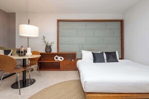 Ein Hotelzimmer mit einem Bett, einem Schreibtisch mit Lampe, einem Sessel, einem kleinen Tisch und einer Zimmerpflanze.