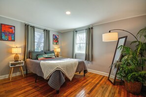 A bedroom with a bed, two bedside lamps, a nightstand, a large mirror, and a potted plant.