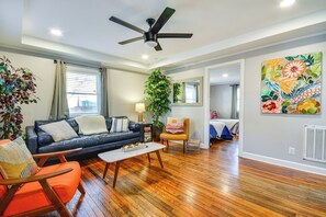 A living room with a sofa, armchair, coffee table, ceiling fan, and a large window with curtains.