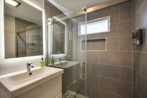 A modern bathroom with a glass-enclosed shower, a large mirror, and a white sink.