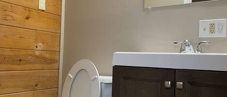 Een badkamer met een houten wand, een wit toilet, een donker houten kastje en een spiegel boven de wastafel.
