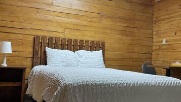 A wooden-paneled room with a bed, a nightstand, and a table.