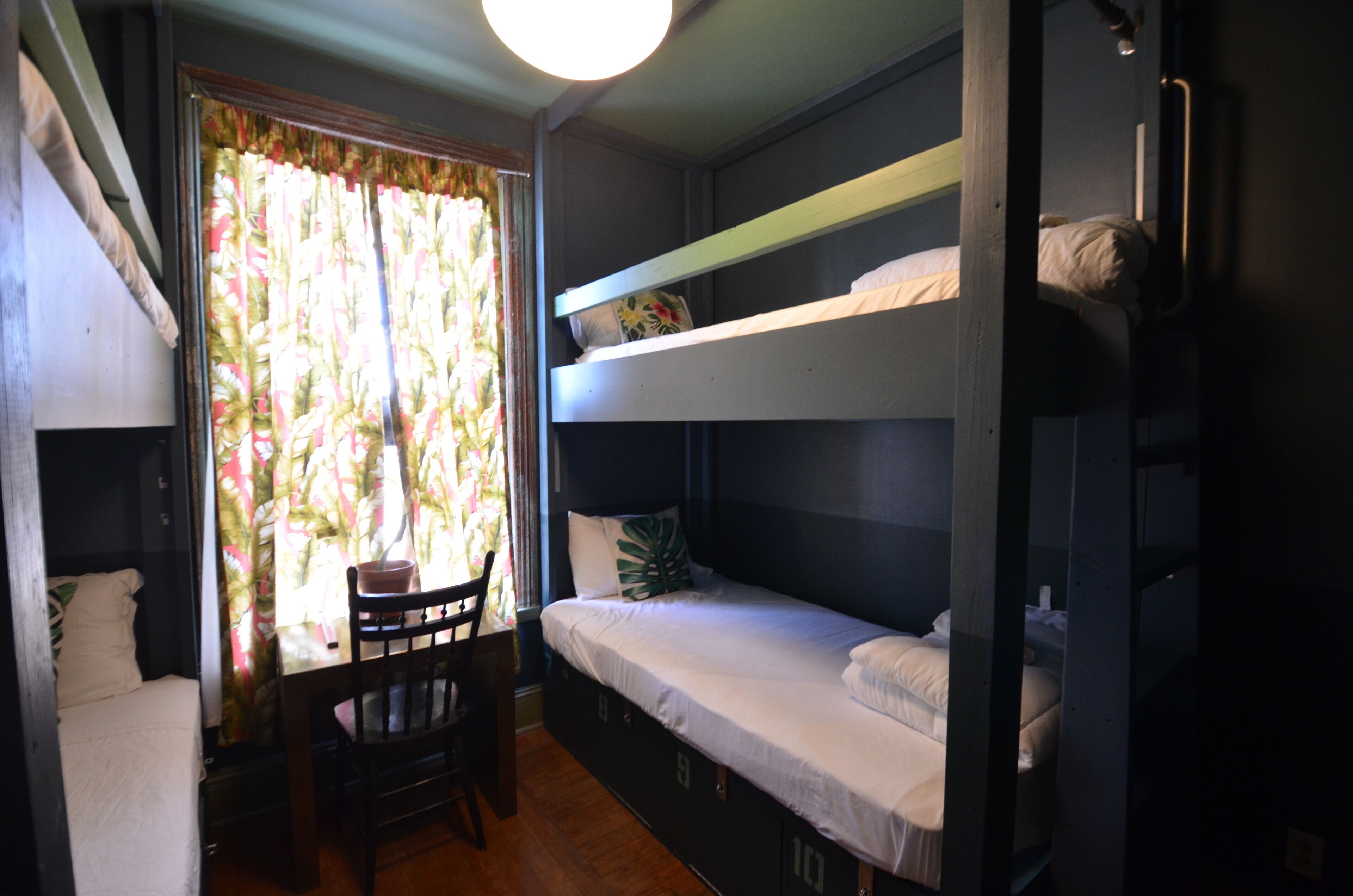 A dormitory room with bunk beds, a wooden chair, and a window with curtains.