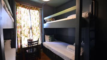 A dormitory room with bunk beds, a wooden chair, and a window with curtains.