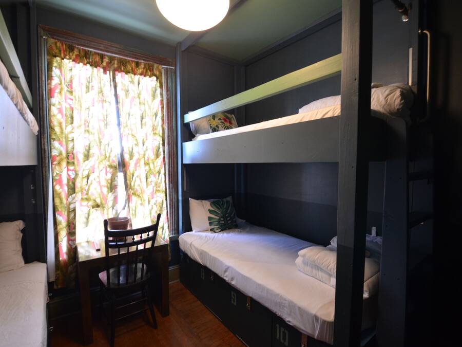 A dormitory room with bunk beds, a wooden chair, and a window with curtains.