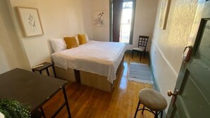 A bedroom with a bed, a chair, a table, and a door. - Michie Hostel (Providence)