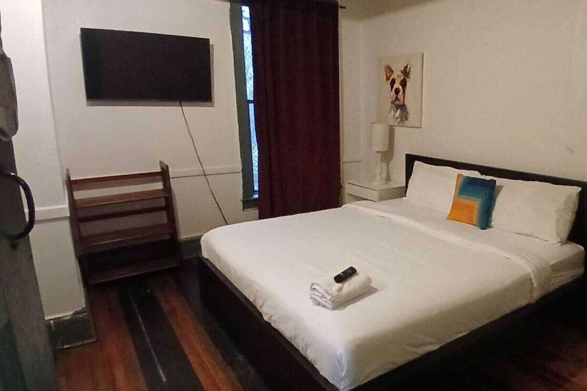 A hotel room with a bed, a chair, a nightstand, a lamp, and a painting on the wall.