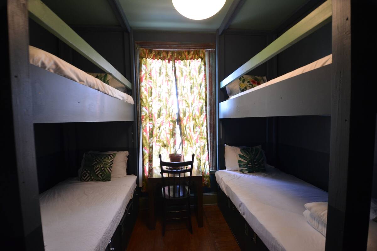 A room with two bunk beds, a small table with a chair, and a window with curtains.