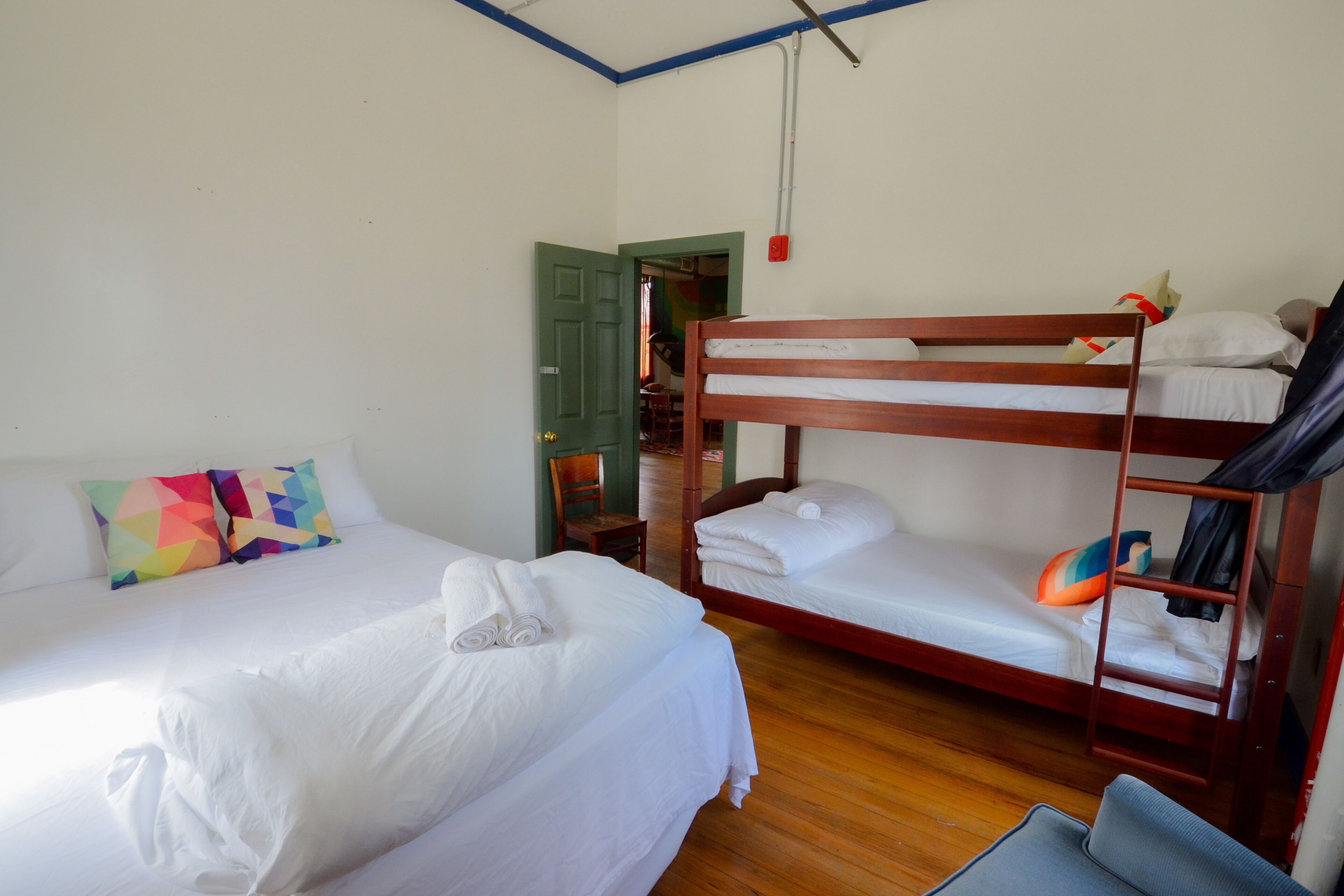 A room with two beds, one with colorful pillows and the other with white bedding.