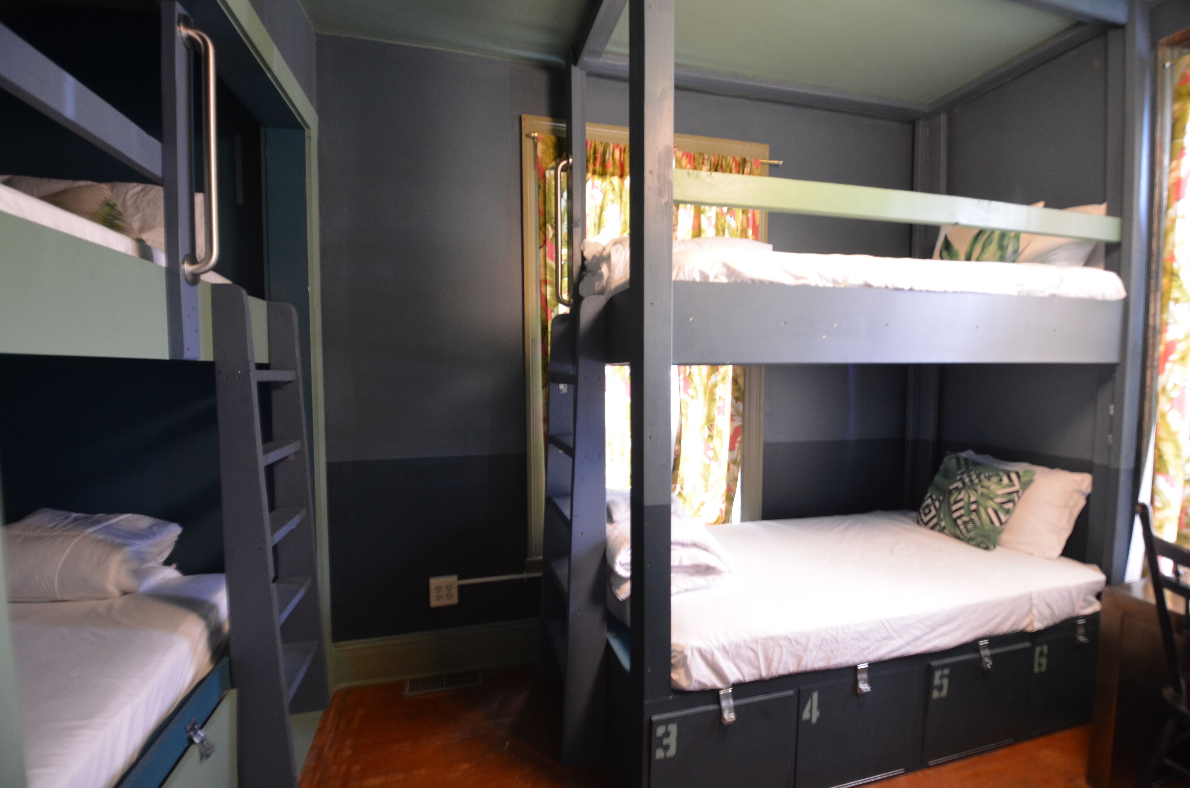 A bunk bed room with a window, curtains, and a small table.