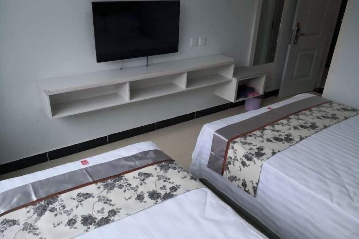 Una habitación de hotel con dos camas, un televisor sobre una estantería blanca y una puerta a la derecha.