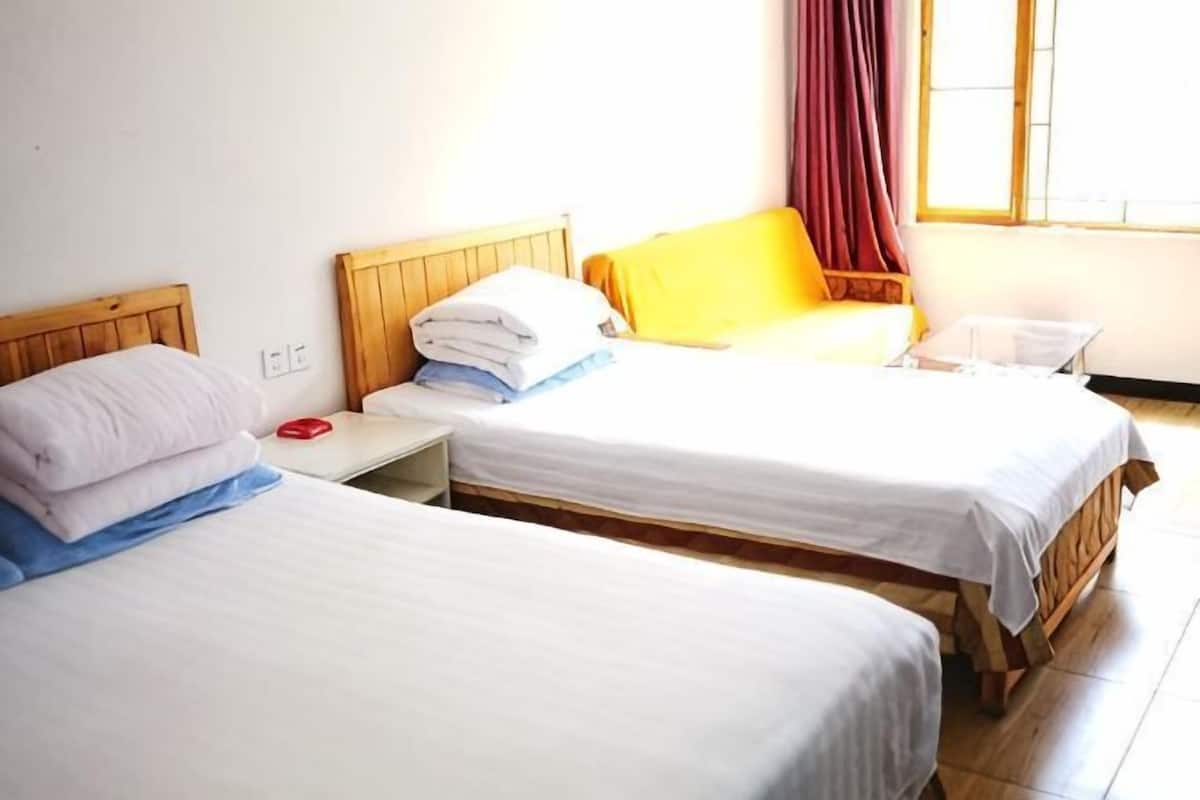 Dos camas individuales con cabeceros de madera, una mesita de noche con un objeto rojo y una ventana con cortinas.
